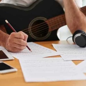 Songwriter with acoustic guitar and writing lyrics on a piece of paper.
