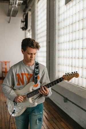 Teen aged boy standing and playing electric guitar.